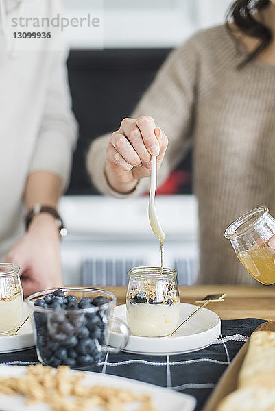 Mitschnitt einer Frau  die Honig in Joghurt mischt  während sie mit ihrem Freund am Tisch steht