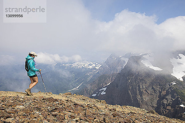 Seitenansicht einer Wanderin mit Wanderstock beim Wandern auf einem Berg vor bewölktem Himmel