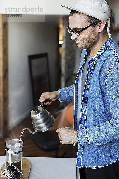 Mann gießt zu Hause kochendes Wasser in Kaffee