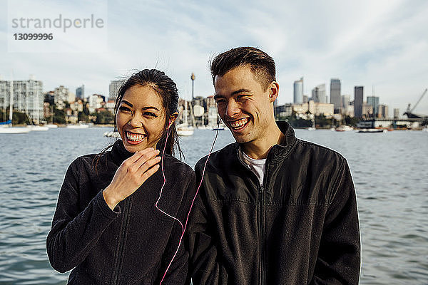 Glückliches junges Paar hört Musik  während es gegen das Stadtbild trainiert