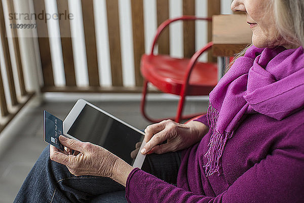 Schrägansicht einer älteren Frau beim Online-Shopping  die auf einem Stuhl auf der Veranda sitzt