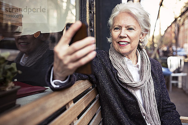 Lächelnde ältere Frau benutzt Smartphone  während sie auf einer Bank sitzt