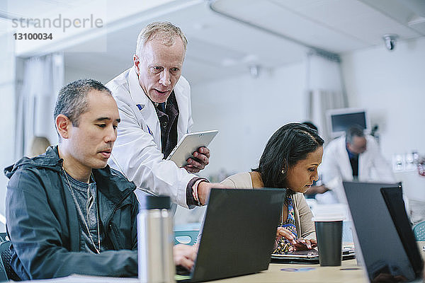 Männlicher Arzt diskutiert mit Kollegen über Laptop-Computer im Behandlungszimmer