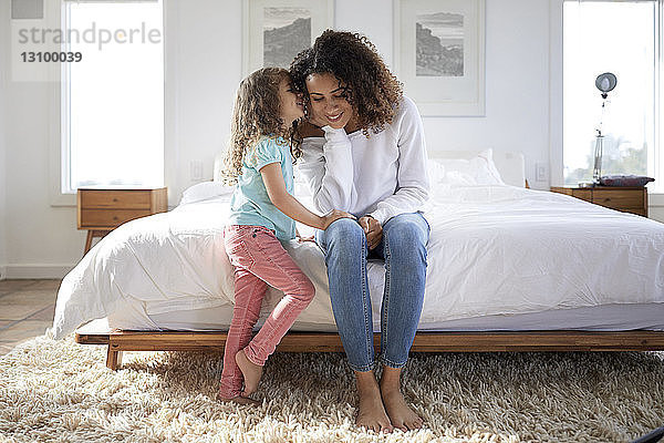 Tochter flüstert der zu Hause im Bett sitzenden Mutter zu