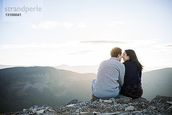 Rückansicht eines auf Felsen sitzenden Paares am Bergfelsen