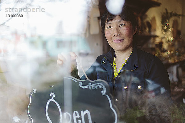 Weiblicher Eigentümer hängt offenes Schild am Fenster des Gartencenters durch Glas gesehen