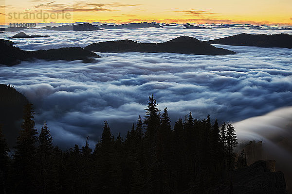 Majestätische Aussicht auf Wolken  die bei Sonnenuntergang Berge bedecken