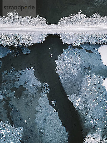 Hochwinkel-Distanzansicht einer Person  die im Winter auf einem See bei einer Brücke paddelt