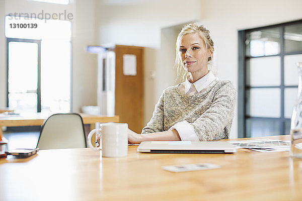 Porträt einer selbstbewussten Geschäftsfrau am Tisch sitzend mit Laptop-Computer im Büro