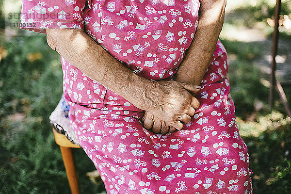 Mitschnitt einer älteren Frau mit gefalteten Händen im Hinterhof sitzend