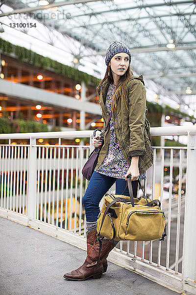 Frau in voller Länge mit Gepäck lehnt am Flughafen auf dem Geländer