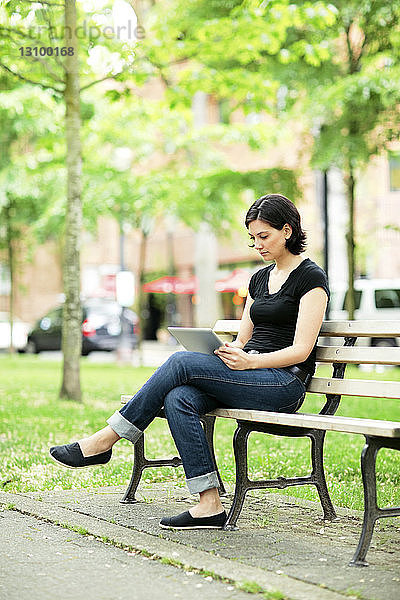 Junge Frau benutzt Tablet-Computer  während sie auf einer Parkbank sitzt