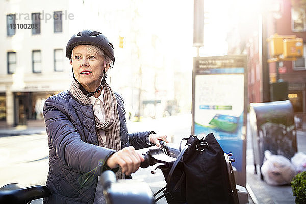 Nachdenkliche ältere Frau sitzt auf dem Fahrrad auf der Straße
