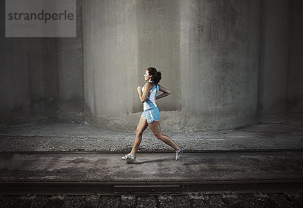 Entschlossene Sportlerin joggt auf einem Fußweg an einer Eisenbahnschiene