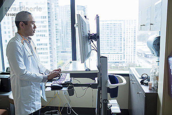 Männlicher Arzt benutzt Desktop-Computer  während er auf der Krankenhausstation steht