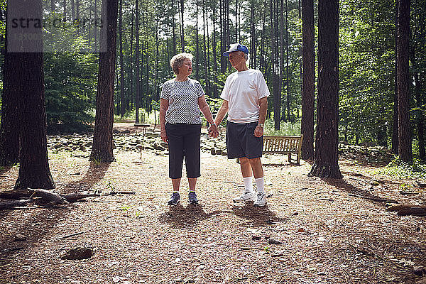 Älteres Ehepaar hält im Wald Händchen und steht dabei im Wald