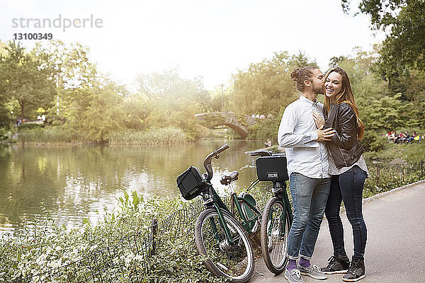 Mann küsst im Stehen mit Fahrrädern am See seine Freundin