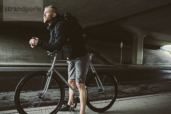 Männlicher Pendler mit Fahrrad  der auf der Brücke stehend wegschaut