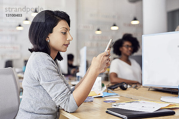Geschäftsfrau benutzt Smartphone mit einer Kollegin im Hintergrund