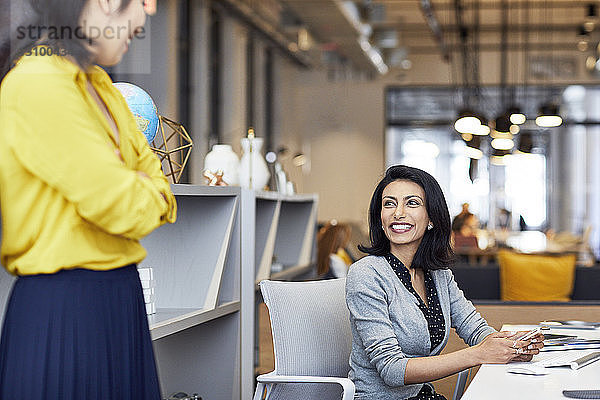 Glückliche Geschäftsfrau betrachtet Kollegin  während sie im Kreativbüro sitzt