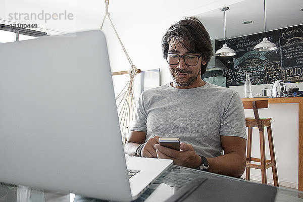 Mann benutzt Smartphone  während er zu Hause sitzt