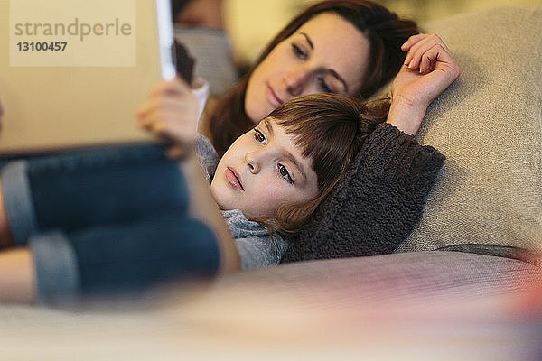 Mutter und Tochter benutzen Tablet-Computer  während sie zu Hause auf dem Sofa liegen
