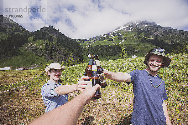 Glückliche Freunde stoßen auf dem Feld gegen Berge und bewölkten Himmel auf Bierflaschen an