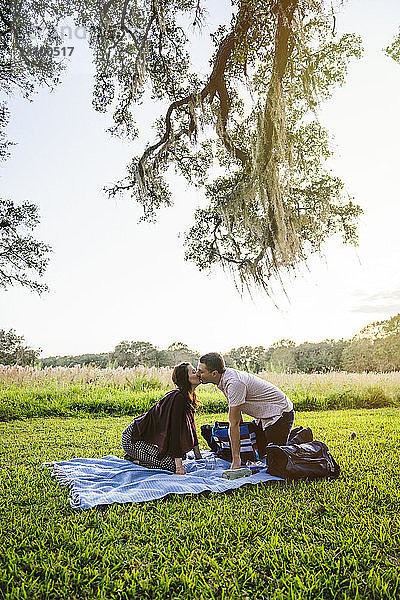Seitenansicht eines Paares  das sich kniend auf einer Decke im Park küsst