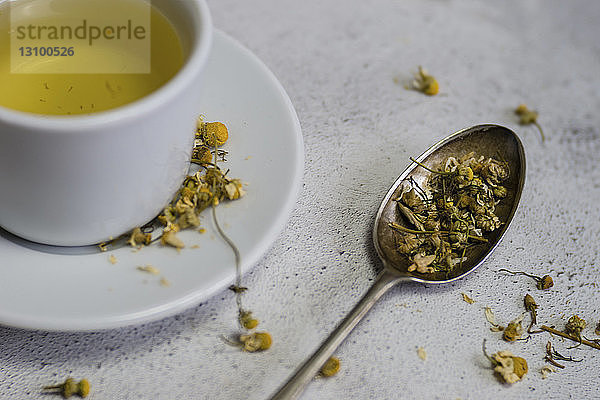 Hochwinkelansicht von Kamillentee in Tasse und Löffel auf dem Tisch