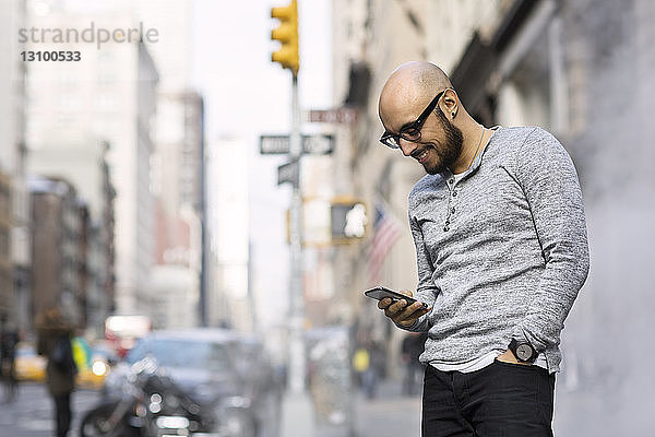 Glücklicher Mann benutzt Smartphone  während er auf der Straße steht