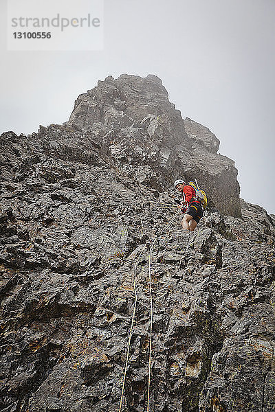 Niedrigwinkelansicht eines sportlichen Wanderers  der Berg gegen Himmel klettert
