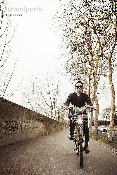Frontansicht eines lächelnden Mannes beim Fahrradfahren auf der Straße bei klarem Himmel