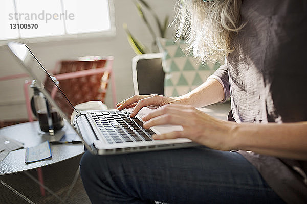 Mittelsektion einer Frau  die zu Hause im Wohnzimmer einen Laptop benutzt