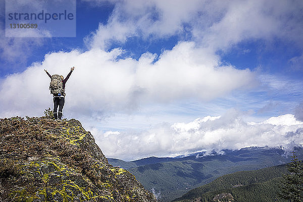 Tiefwinkelansicht einer Frau  die mit erhobenen Armen auf einem Berg vor bewölktem Himmel steht