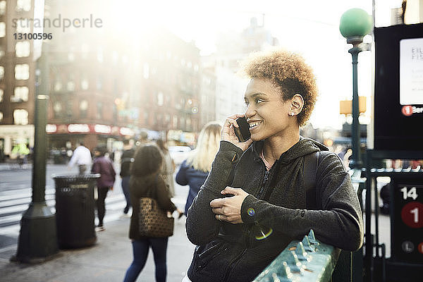Glückliche junge Frau  die an einem sonnigen Tag ein Smartphone auf dem Bürgersteig benutzt