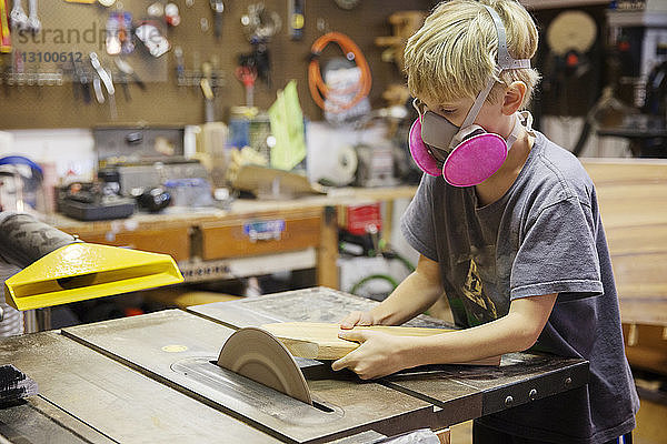 Junge schneidet Holz mit der Tischsäge in der Werkstatt