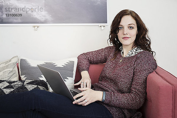Porträt einer Geschäftsfrau  die auf dem Sofa sitzend einen Laptop benutzt