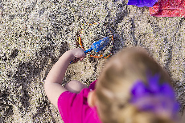 Draufsicht auf ein Mädchen  das am Strand mit Sand spielt