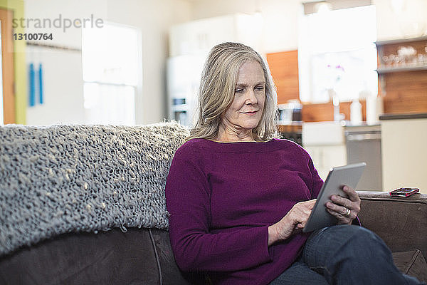 Ältere Frau benutzt Tablet-Computer  während sie zu Hause auf dem Sofa sitzt
