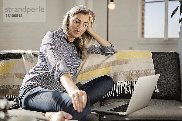Entspannte Frau mit Laptop auf Sofa sitzend