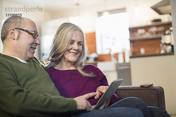 Lächelndes Paar benutzt Tablet-Computer  während es zu Hause auf dem Sofa sitzt