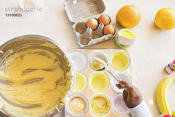 Ausgeschnittenes Bild eines Mädchens  das Teig in einen Cupcake-Halter füllt