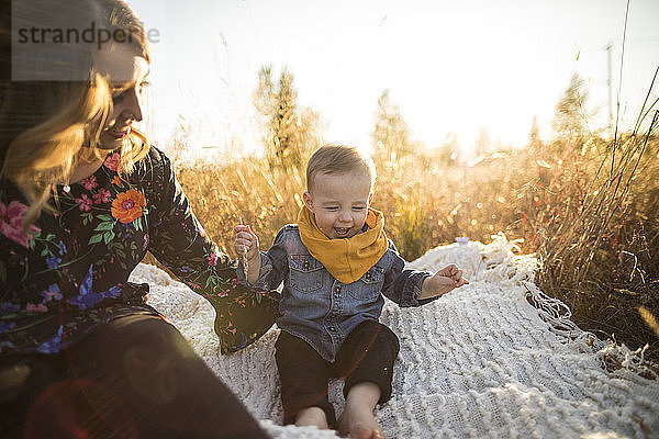 Mutter schaut auf glücklichen Sohn  der auf einer Picknickdecke auf dem Feld sitzt