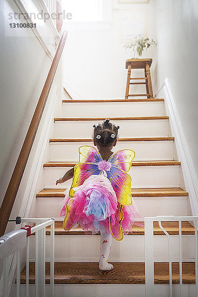 Rückansicht eines märchenhaft gekleideten Mädchens  das zu Hause die Treppe hinaufgeht