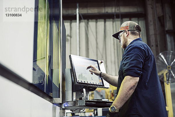 Niedrigwinkelansicht eines Arbeiters mit Desktop-Computer bei der Arbeit in einer Stahlfabrik