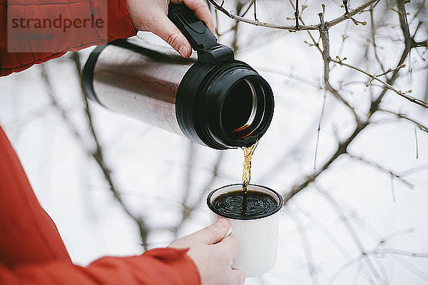 Nahaufnahme einer Frau  die im Winter schwarzen Kaffee aus einem isolierten Getränkebehälter in einen Becher gießt