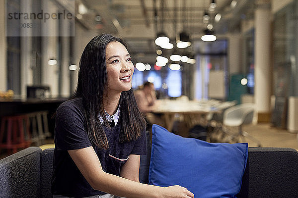 Nachdenklich lächelnde Geschäftsfrau sitzt auf Sofa im Kreativbüro