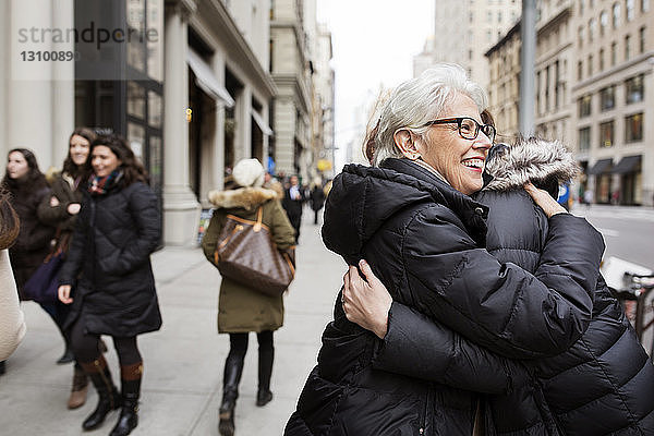 Fröhliche Frauen umarmen sich auf dem Fußweg in der Stadt