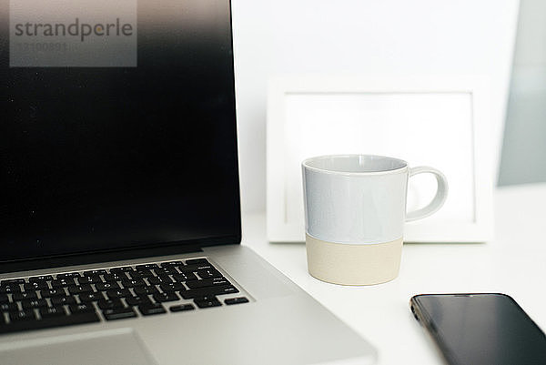 Nahaufnahme einer Kaffeetasse mit einem Laptop auf dem Schreibtisch