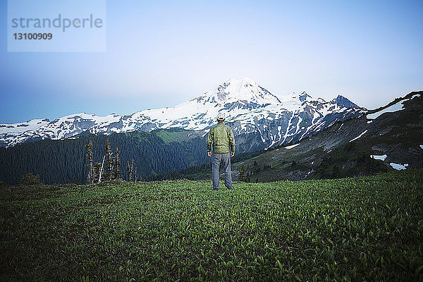 Rückansicht eines Mannes  der auf einem Grasfeld gegen einen Berg steht